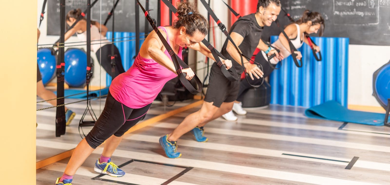 Varias personas entrenan con cintas de suspensión en la sala de un gimnasio